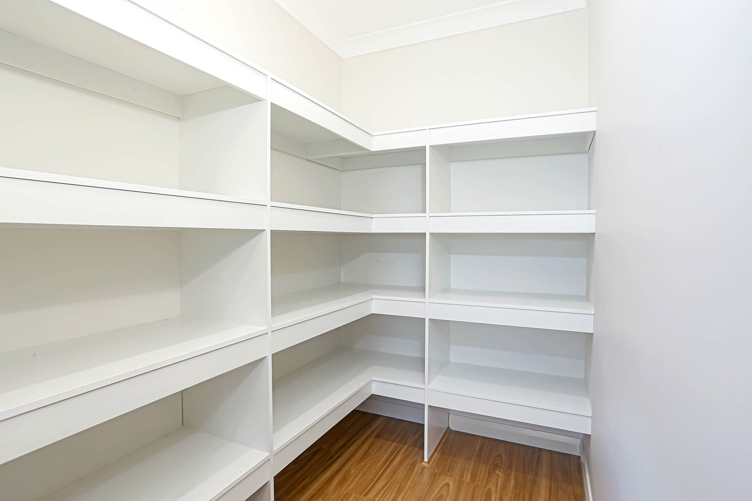 A Walk In Closet With White Shelves And Wooden Floors
